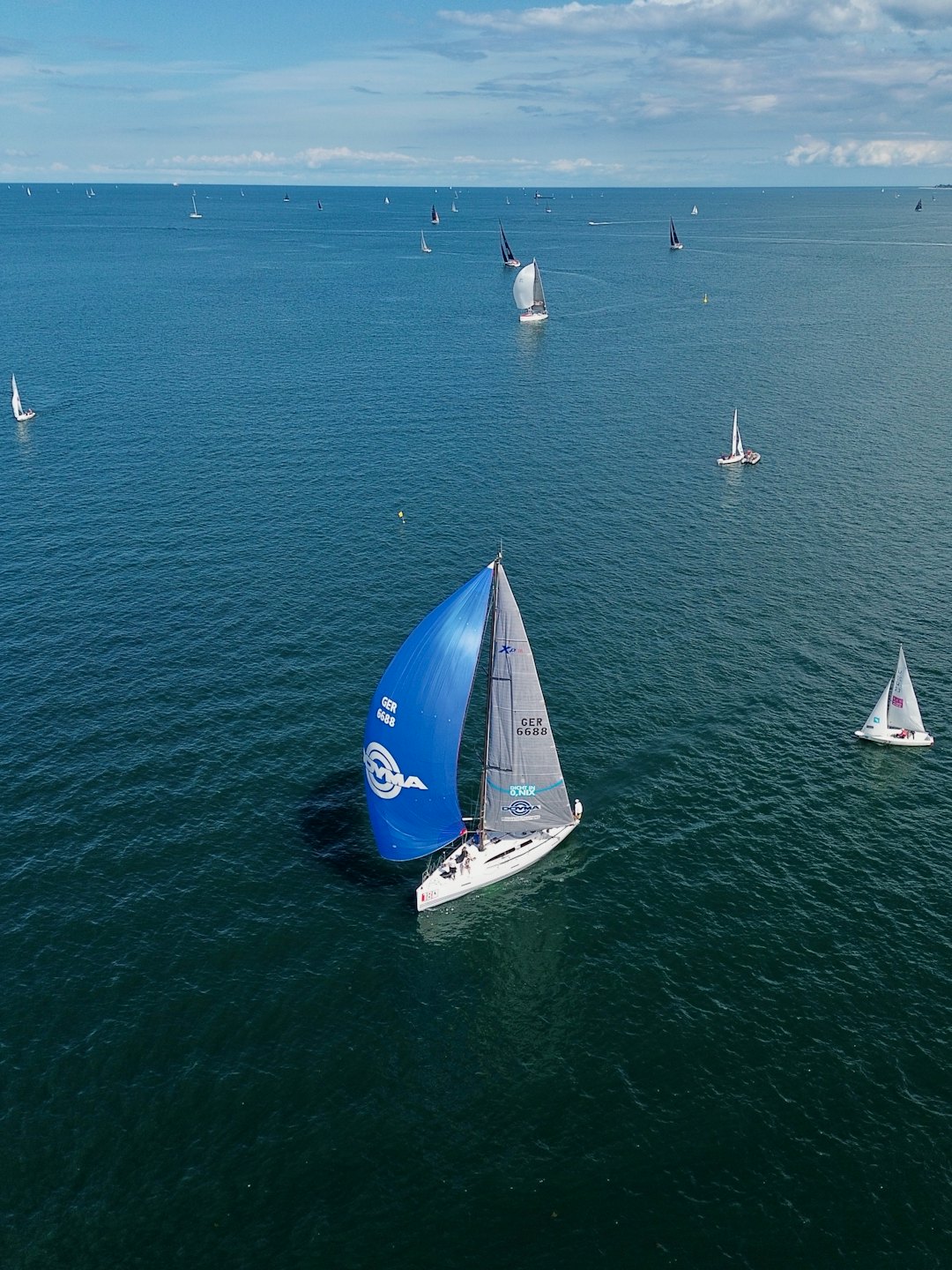 Una barca a vela bianca con uno spinnaker blu guida una regata.
