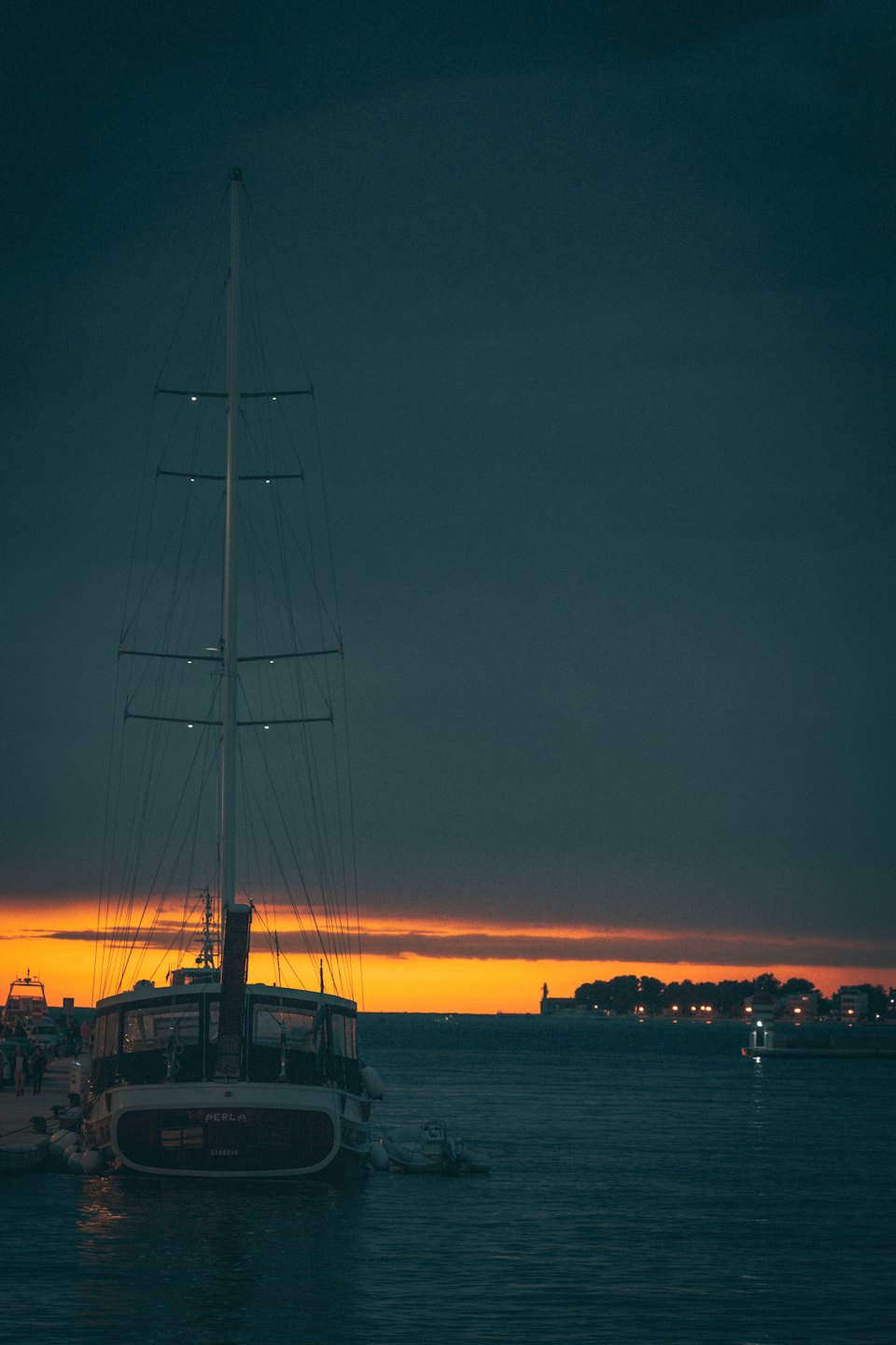 Una barca a vela con un albero alto è ormeggiata in un porto.