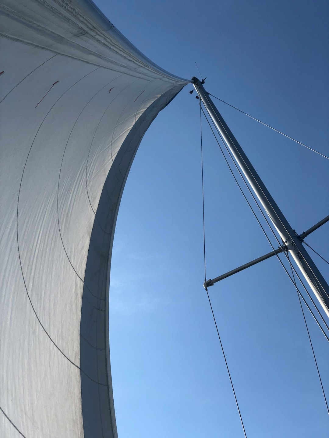 Una grande vela bianca di una barca a vela si gonfia contro un cielo limpido.