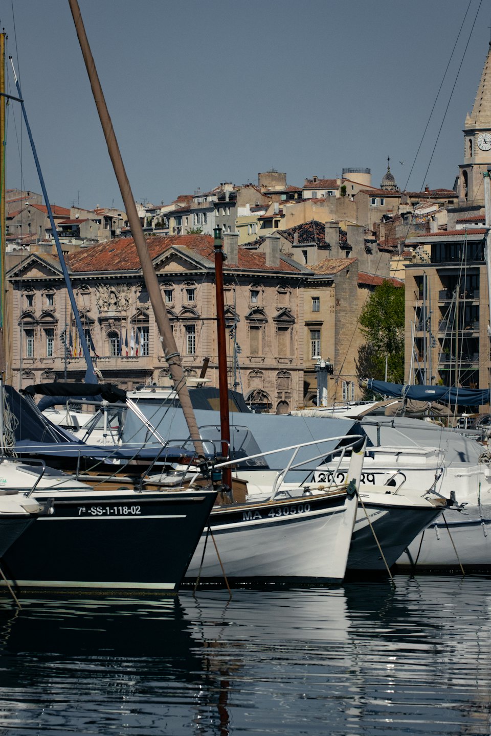 Barche a vela ormeggiate in un porto turistico di fronte a un paesaggio urbano europeo.